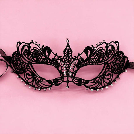 Masque vénitien noir Midnight Lace en dentelle ajourée avec arabesques et strass, sur fond rose pastel.