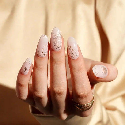 Ongles nude au style céleste avec motifs soleil, lune et étoiles en doré, pour une manucure chic signée EMANO
