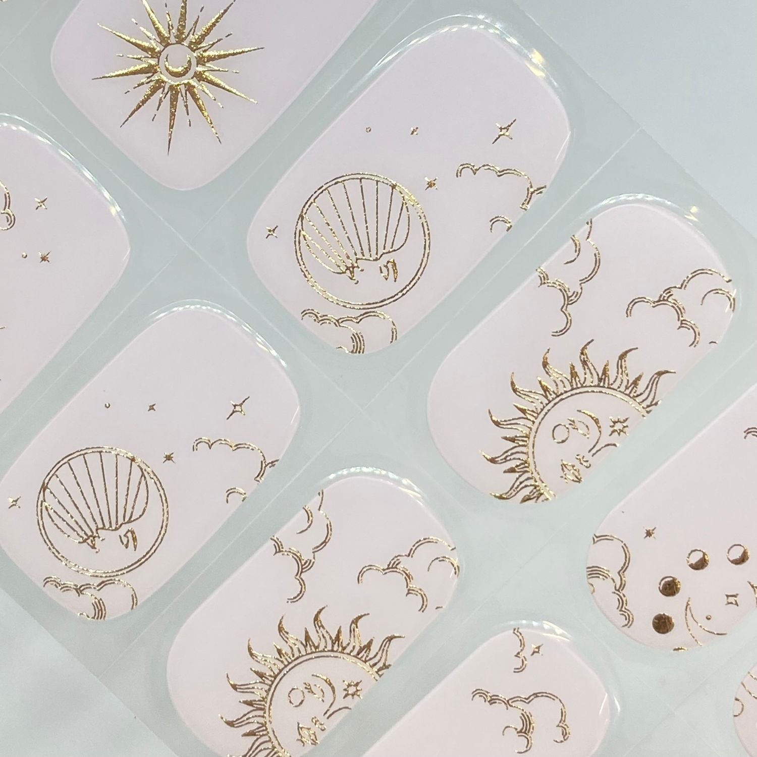 Ongles nude au style céleste avec motifs soleil, lune et étoiles en doré, pour une manucure chic signée EMANO