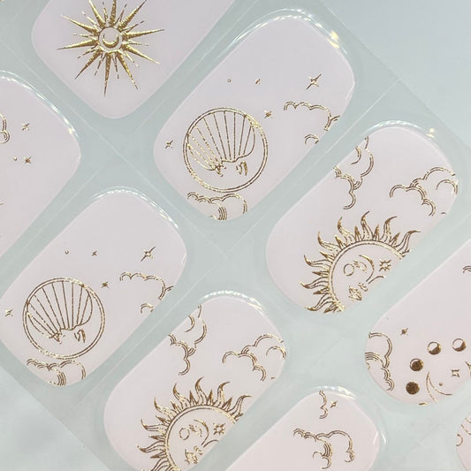 Ongles nude au style céleste avec motifs soleil, lune et étoiles en doré, pour une manucure chic signée EMANO